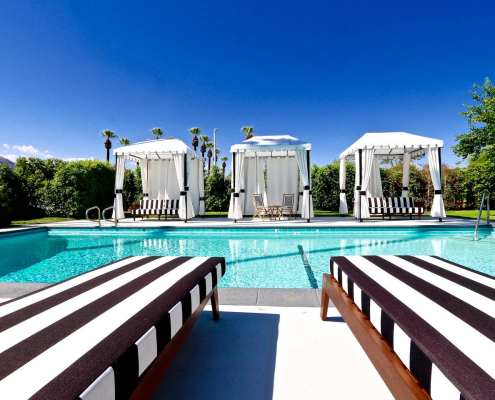 Black and white striped lounge chairs in front of the pool and next to three outdoor cabanas at Hotel El Cid in Palm Springs, California