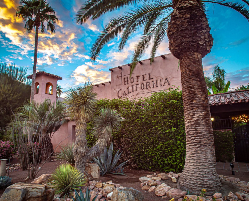 The front of Hotel California with a palm tree in the foreground and another palm in the background at sunset on a cloudy day