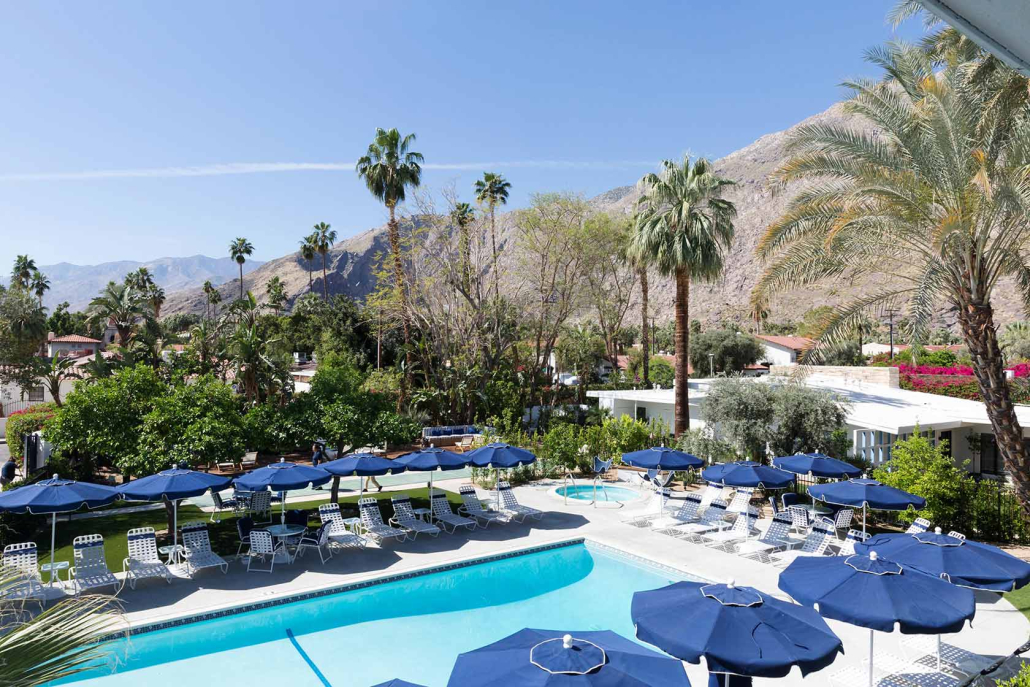 Blue umbrellas and palms surround the large pool at Holiday House in Palm Springs, California