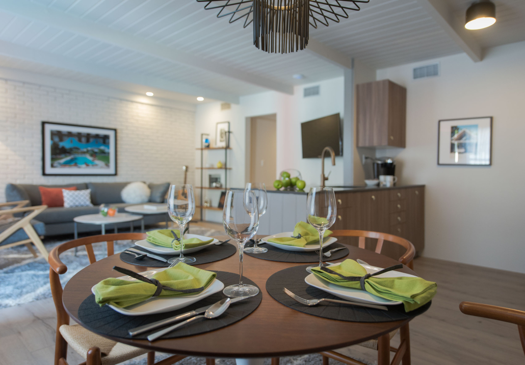 Wine glasses, green napkins, cutlery, and plates on a brown wooden table in the dining area of a room at The Weekend Palm Springs