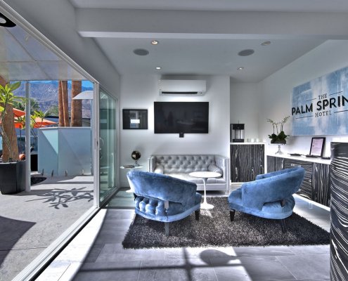 Light blue chairs on a gray rug in front of a large screen television in the lobby of The Palm Springs Hotel