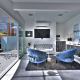 Light blue chairs on a gray rug in front of a large screen television in the lobby of The Palm Springs Hotel