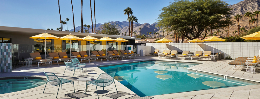 Bright yellow umbrellas shade loungers around the beautiful large pool at Twin Palms men's clothing-optional resort in Palm Springs, California