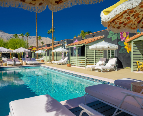 The pool surrounded by white loungers and umbrellas at Fleur Noire Hotel in Palm Springs, California