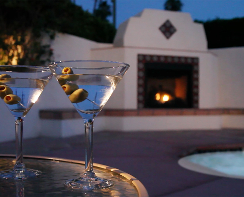 Two martini glasses on a table in front of a fireplace outside at the Hacienda at Warm Sands