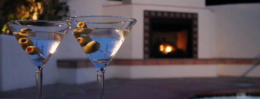 Two martini glasses on a table in front of a fireplace outside at the Hacienda at Warm Sands