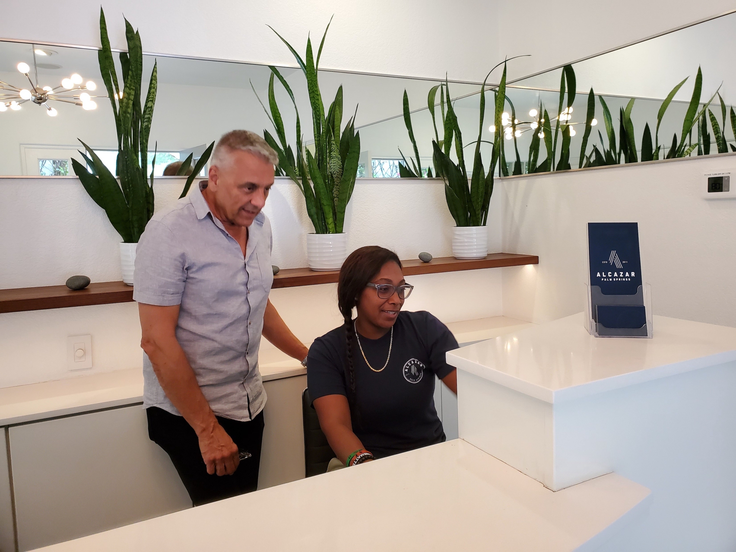 A man and a woman behind the front desk at Alcazar Palm Springs look at a computer