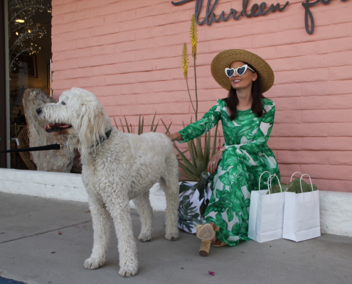 A woman wearing a green dress sits outside of a pink building in Palm Springs with a white dog