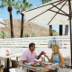 A man and a woman sit at a table outside under an umbrella in Palm Springs, California. Photo courtesy of Visit Palm Springs