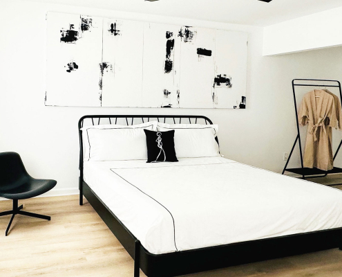 A white comforter on a black bed frame under a black and white artwork at The Jazz Hotel Palm Springs