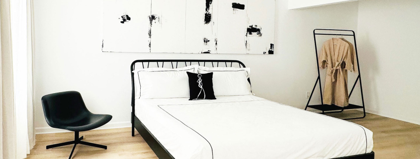 A white comforter on a black bed frame under a black and white artwork at The Jazz Hotel Palm Springs