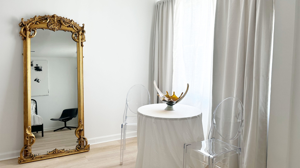 A gilded mirror leans against a white wall next to a small table in a room at Jazz Hotel in Palm Springs, California