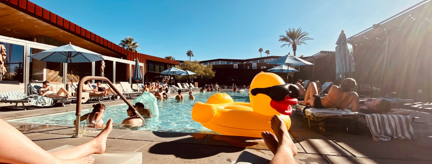 A man relaxes on a chaise lounge by the pool in Palm Springs, California, with a rubber duck float in the water