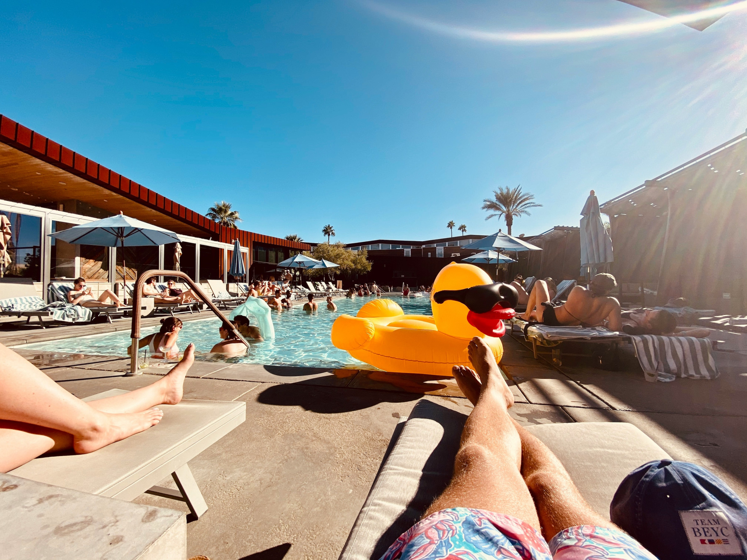 A man relaxes on a chaise lounge by the pool in Palm Springs, California, with a rubber duck float in the water