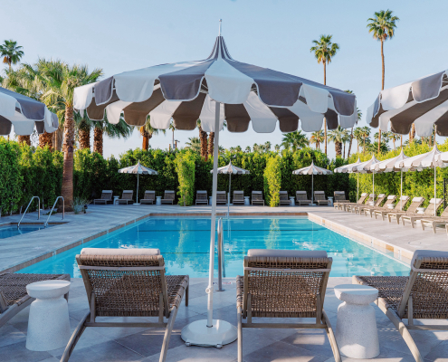 Four lounge chairs and striped umbrellas in front of the pool at Azure Sky Resort in Palm Springs, California