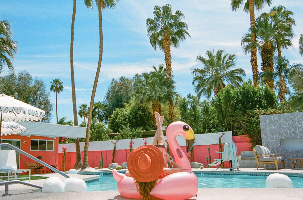 A woman wearing an orange hat lounges in a flamingo pool float at The Muse Hotel Palm Springs
