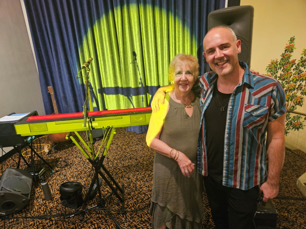 A man in a striped shirt and a woman in a green dress pose in front of a keyboard at the Palm Springs Cultural Center