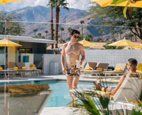 Two men smile at each other while hanging out by the pool on a sunny day at Twin Palms Resort in Palm Springs, California