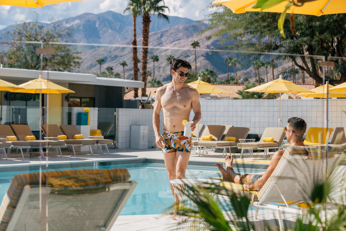 Two men smile at each other while hanging out by the pool on a sunny day at Twin Palms Resort in Palm Springs, California