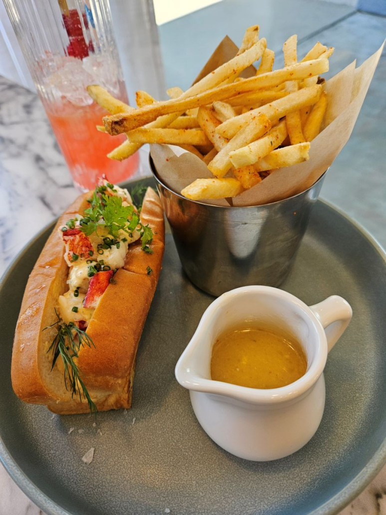 A lobster roll and container of French fries with gravy on a gray plate