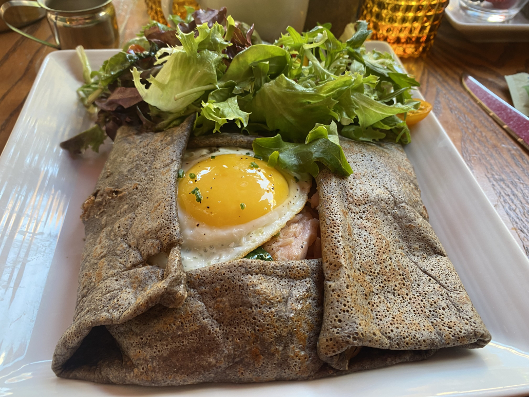 A plate with a salmon and egg crepe on it topped by a salad