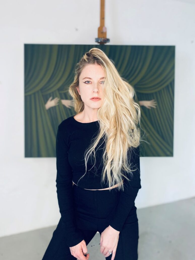 A blonde woman sits in front of a painting