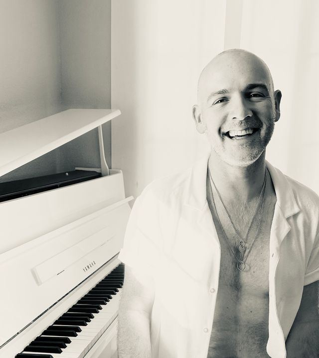 A black and white photo of a smiling bald man sitting at a piano