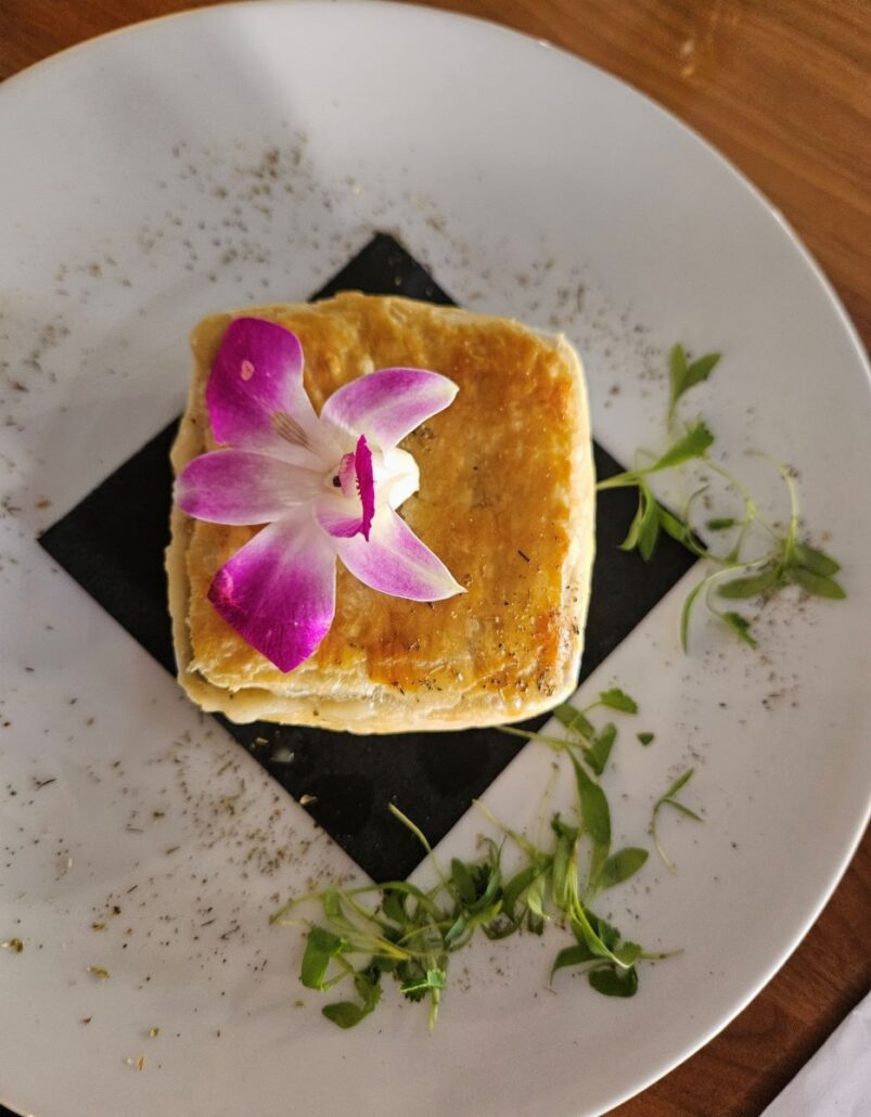 A white plate with chicken pot pie and an orchid decoration