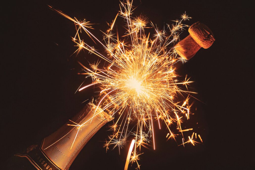 A bottle of Champagne popping with a gold firework. Image by Myriam Zilles on Unsplash
