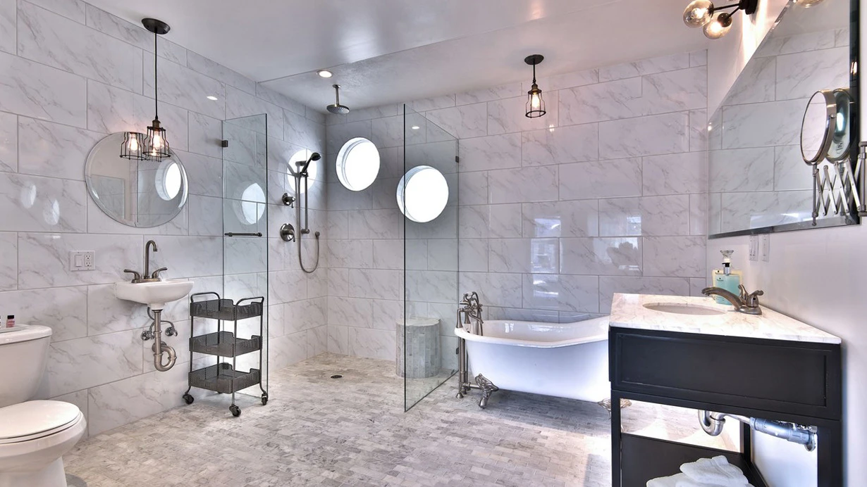 A white marble bathroom with a white bathtub and glass shower at The Palm Springs Hotel