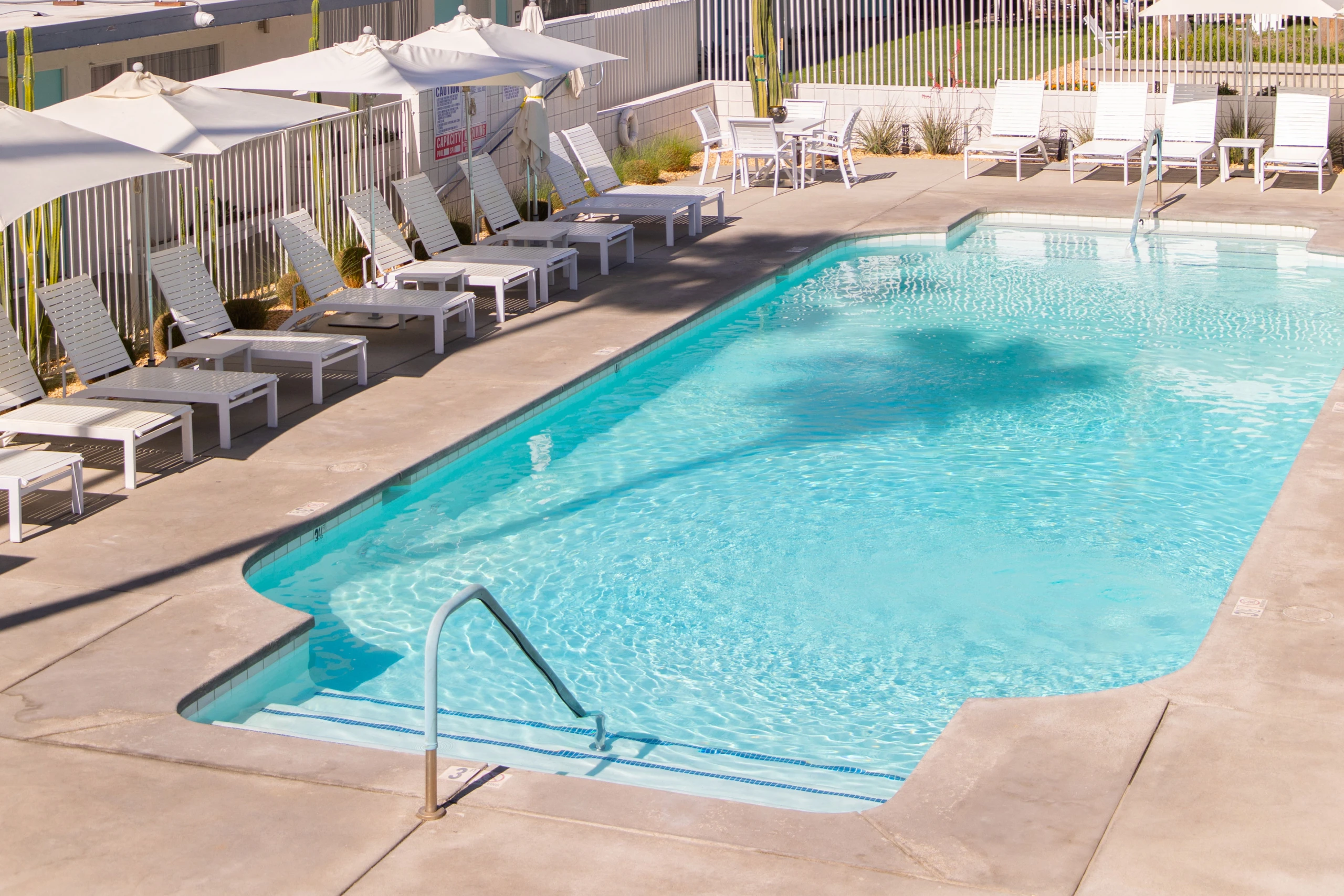 The sparkling blue pool surrounded by white lounge chairs and umbrellas at Skylark Hotel Palm Springs