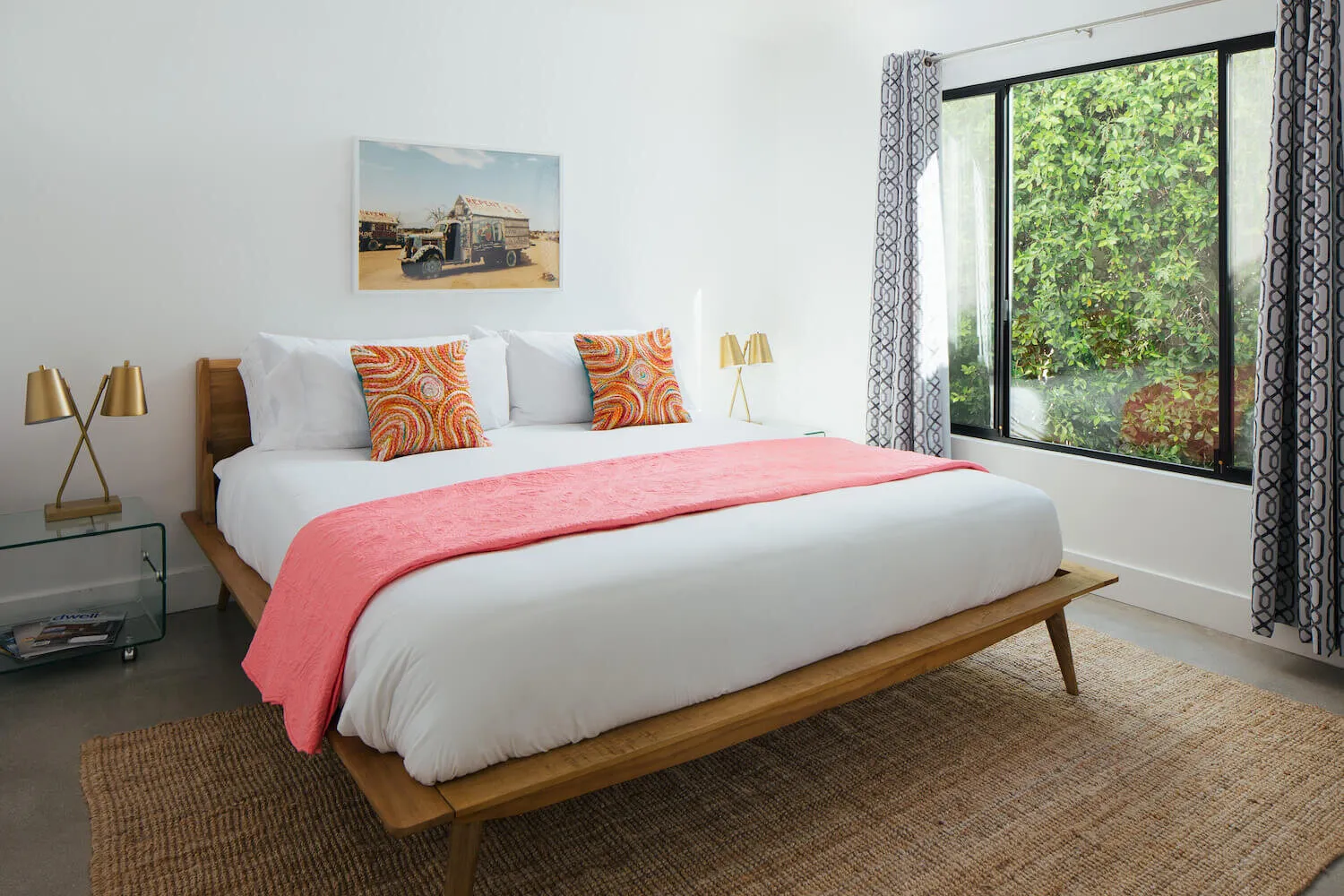 A pink blanket on top of the white bedspread on a bed next to a sliding glass door that leads to the garden outside at Hotel El Cid in Palm Springs, California