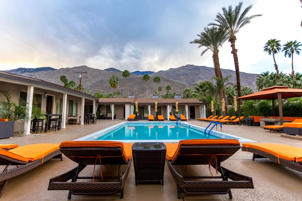 Palm trees and the San Jacinto Mountains are in the background of the Little Paradise Pool and orange loungers in Palm Springs