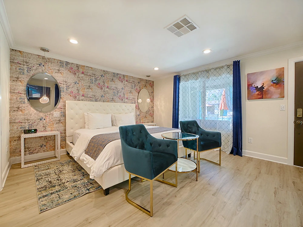 A white bed and teal velvet chair in a light and airy room at The Little Paradise Hotel in Palm Springs, California