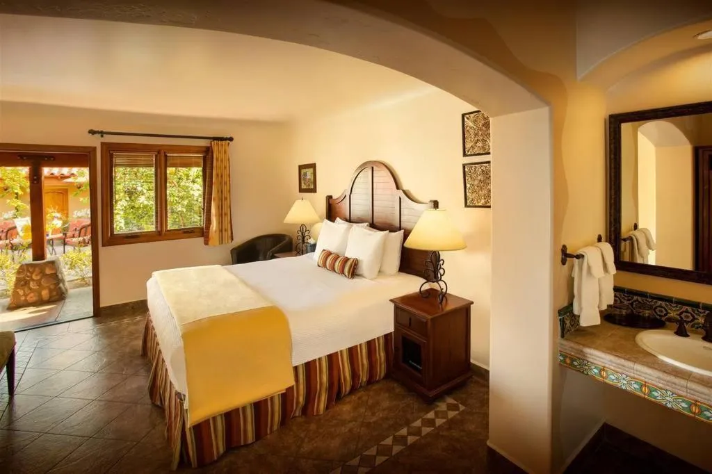 A bed covered with white sheets and a comforter in a spacious room at Los Arboles Hotel in Palm Springs, California
