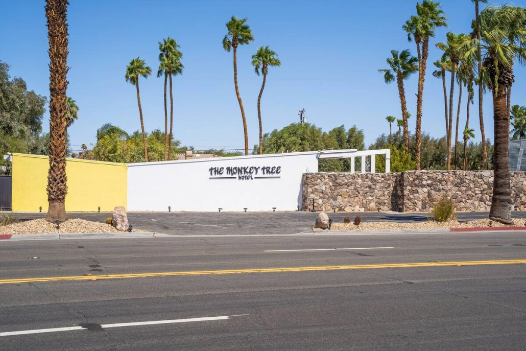 The exterior of The Monkey Tree Hotel with its yellow and white edifice and a rock wall