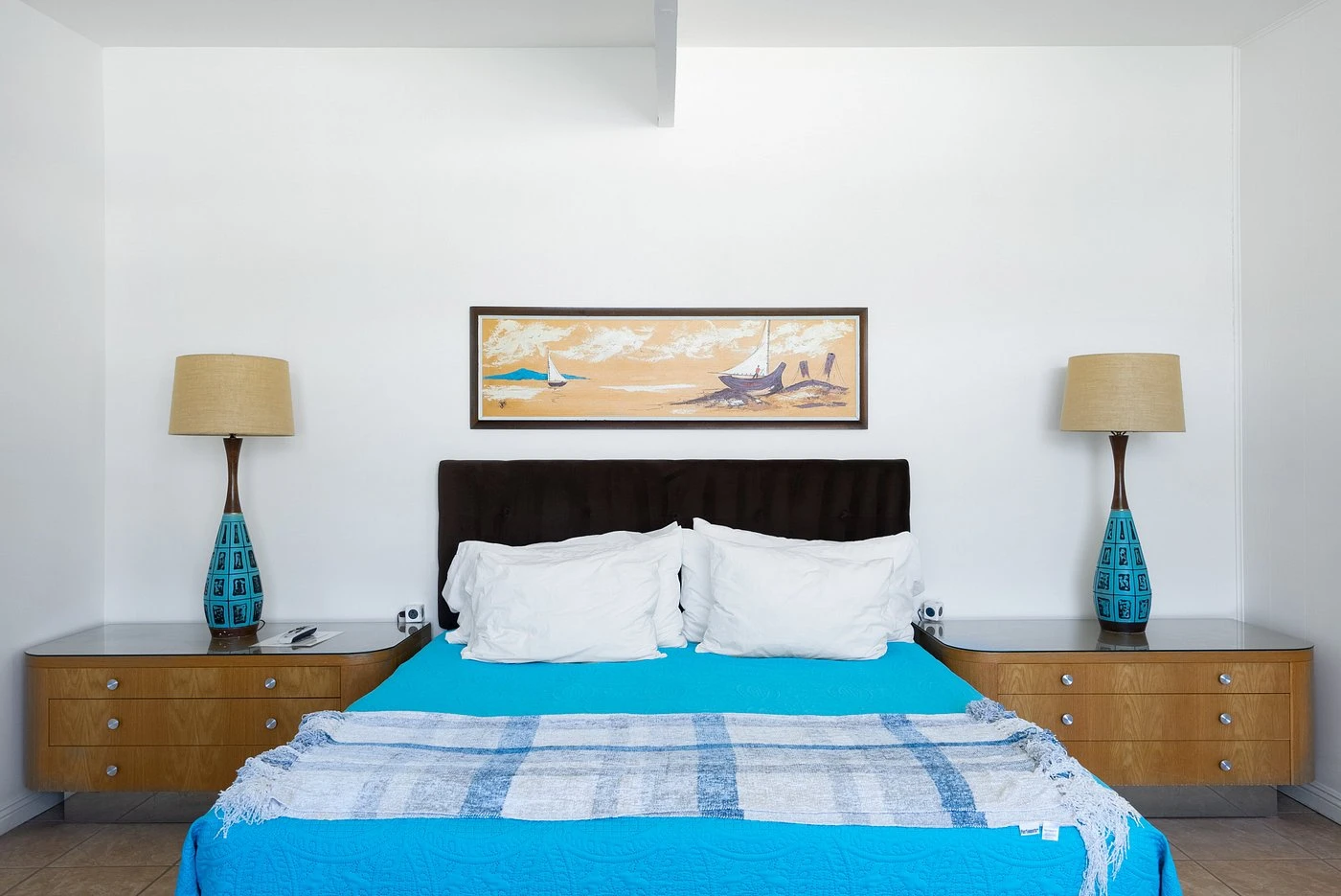 A blue comforter with white pillows and a plaid blanket in a mid-century modern decorated room at The Monkey Tree Hotel in Palm Springs, California