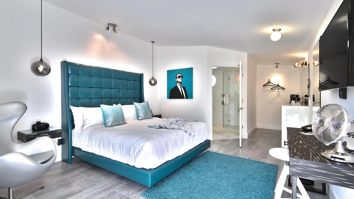 A teal headboard with a bed covered in white sheets on top of a teal rug at The Palm Springs Hotel