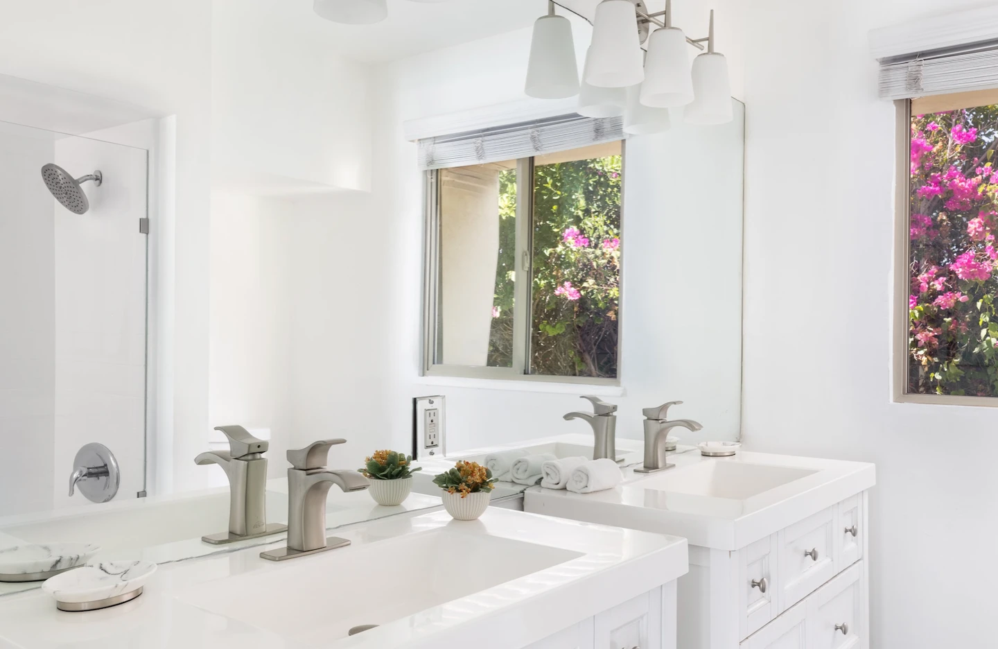 A white tiled bathroom with a sink and faucet and lighting and window with pink flowers at The Three Fifty Hotel in Palm Springs