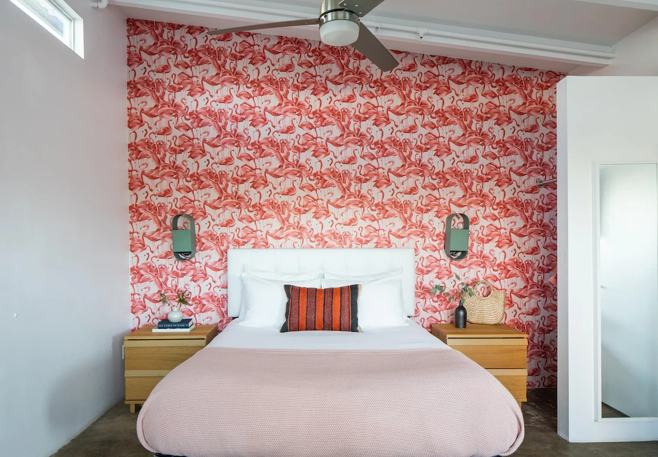 Pink flamingo wallpaper behind a white and pink bed and two wooden nightstands in a bedroom at The Wesley Palm Springs boutique hotel