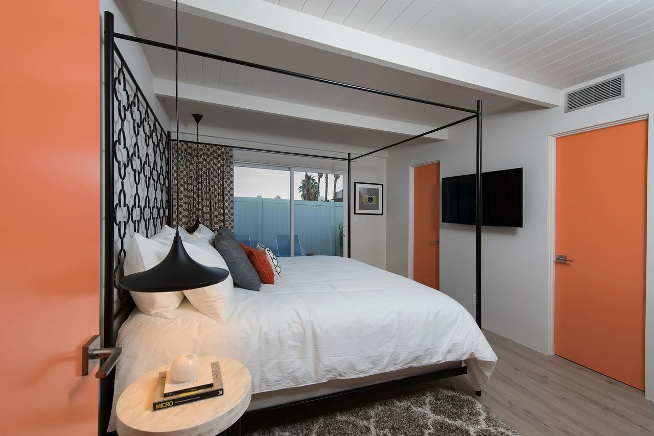 A white bed with red and gray pillows on it next to a hanging pendant light in a bedroom at The Weekend Palm Springs