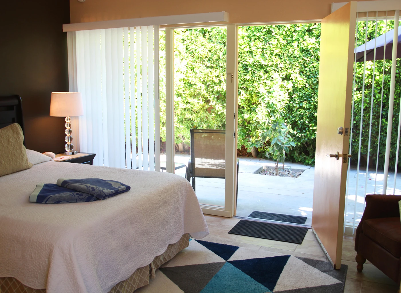 This bedroom at Triangle Inn Palm Springs opens up to a green area with trees and bushes