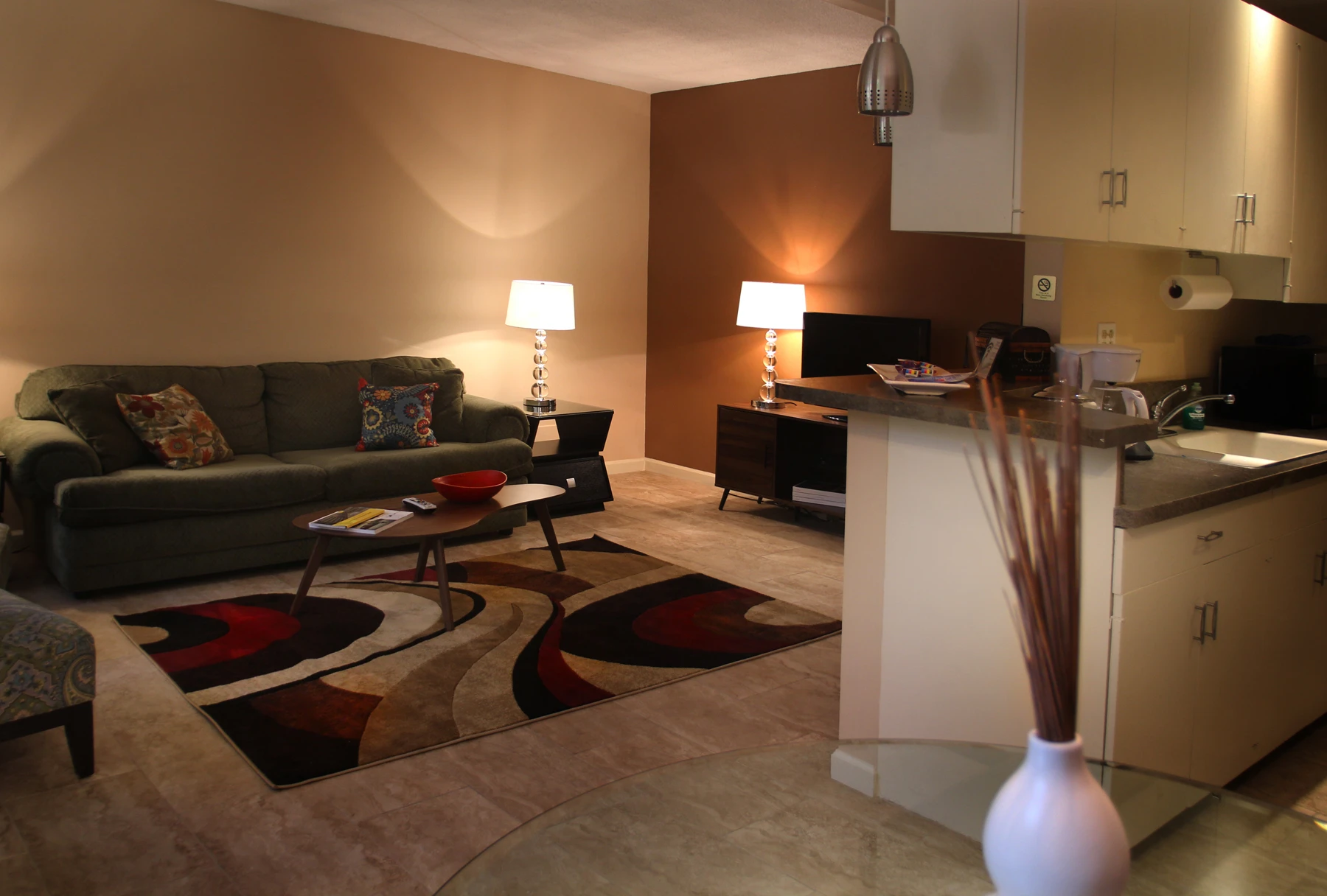 A living room at the Triangle Inn Palm Springs with a large couch and patterned rug on the floor is illuminated by two table lamps