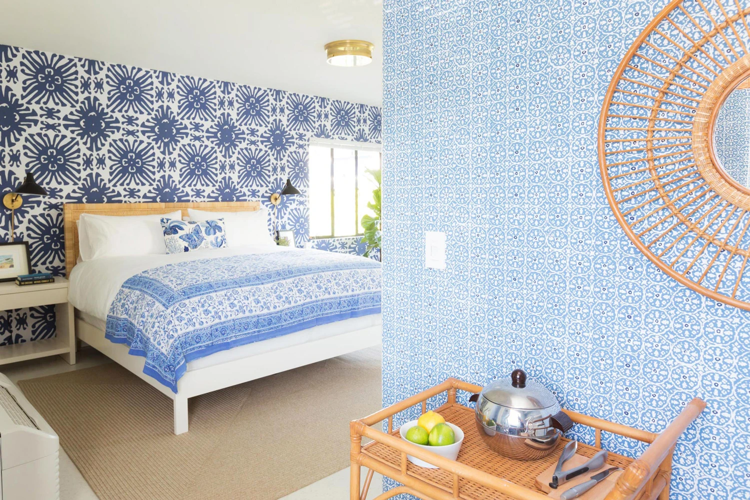 A room at Holiday House Palm Springs with dark blue and white and light blue wallpaper, a white bed with blue comforter, and a bar cart