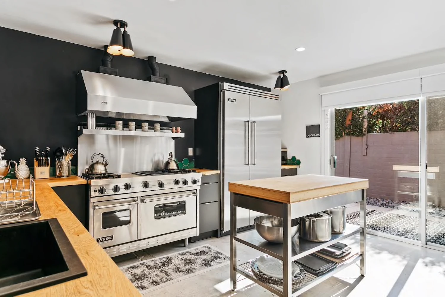 A silver stove and hood next to a butcher block island in the commercial kitchen at The Marley Palm Springs