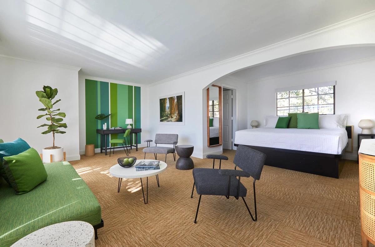 A king-sized bed with white linens and green pillows with a green couch and black chairs at Descanso Resort in Palm Springs
