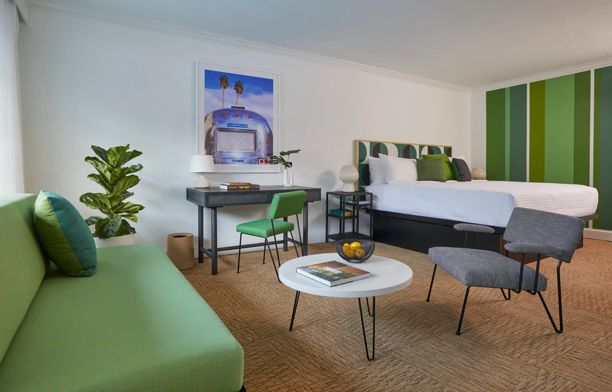 A bed with white linens pops next to the green painted wall and matching couch and desk chair at Descanso Resort Palm Springs