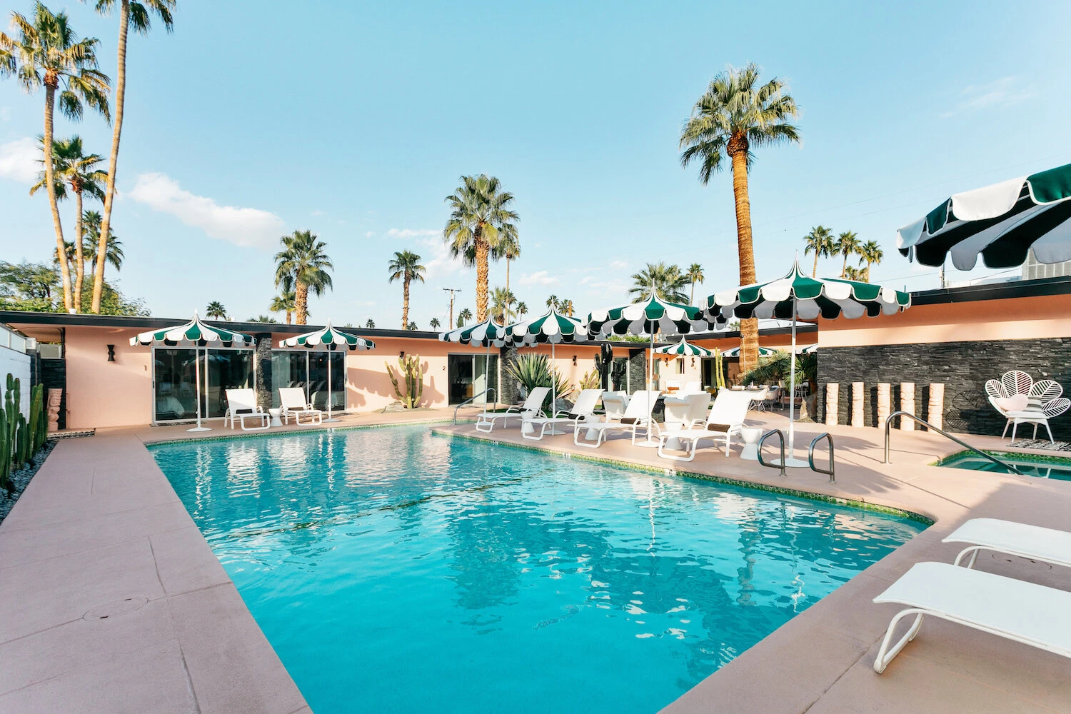 Green and white striped umbrellas and white loungers surround the sparkling pool at The Marley Palm Springs