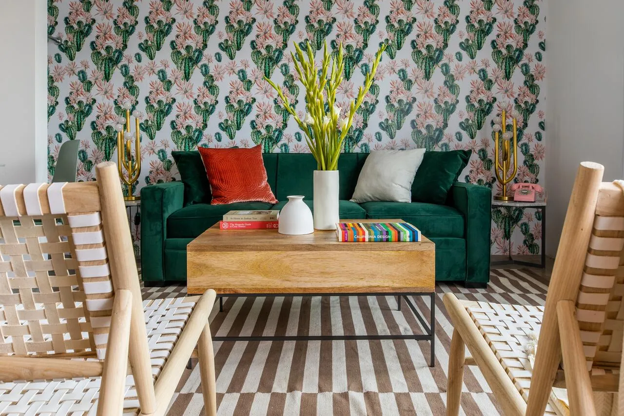 A bold floral cactus wallpaper stand out behind a green velvet couch and wooden table at The Wesley Palm Springs boutique hotel