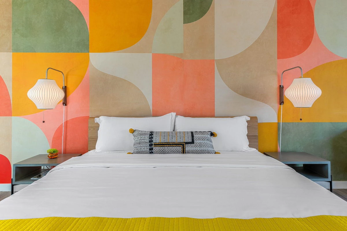 A bright mural behind a white bed at Limón Palm Springs